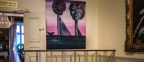 A staircase with a metal railing, a painting of abstract shapes on the wall, and a framed picture to the right.