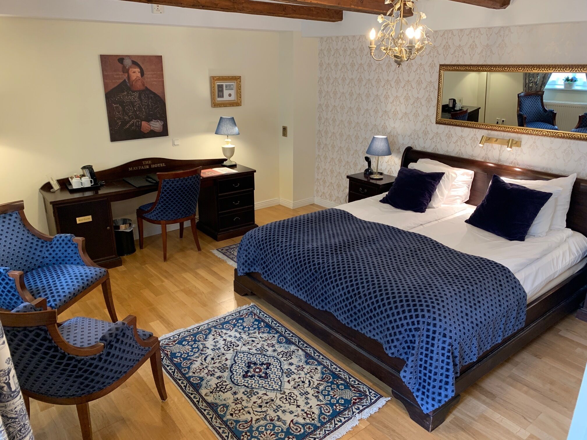 Hotelkamer met een groot bed, een bureau, een stoel, een bureaulamp, een nachtkastje, een spiegel en een kamerkleed met dessin.