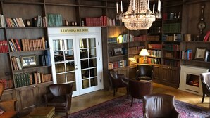 A library with bookshelves, leather chairs, a chandelier, and a fireplace. - Mayfair Hotel Tunneln (Malmö)