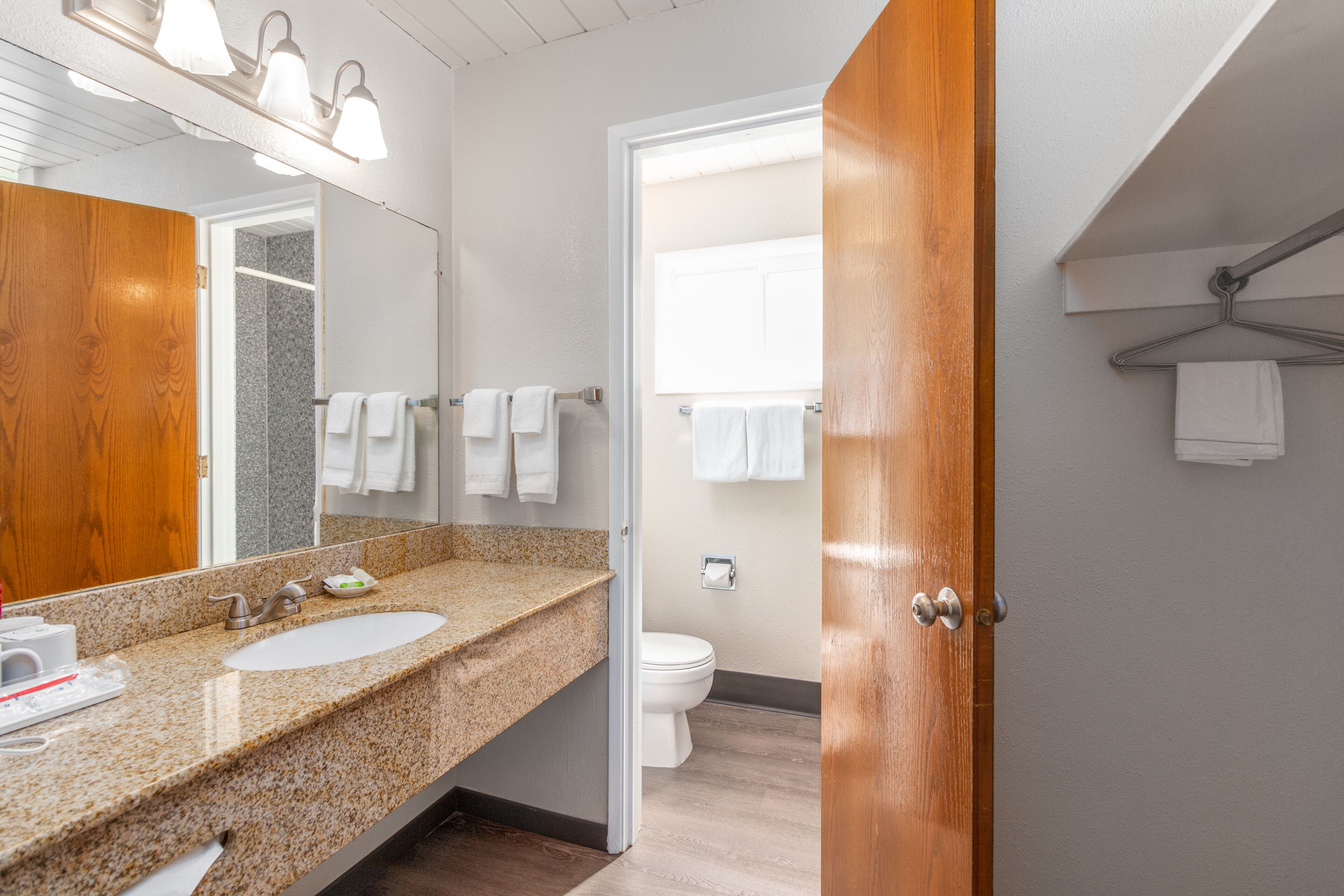 A modern bathroom with a granite countertop sink, a mirror, and a wooden door.