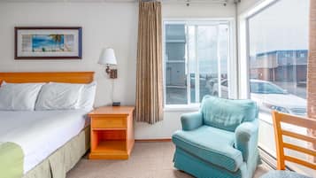 Ein Hotelzimmer mit Bett, Nachttisch, Lampe, Stuhl, einem Fenster mit Blick auf Autos und einem Bild an der Wand.