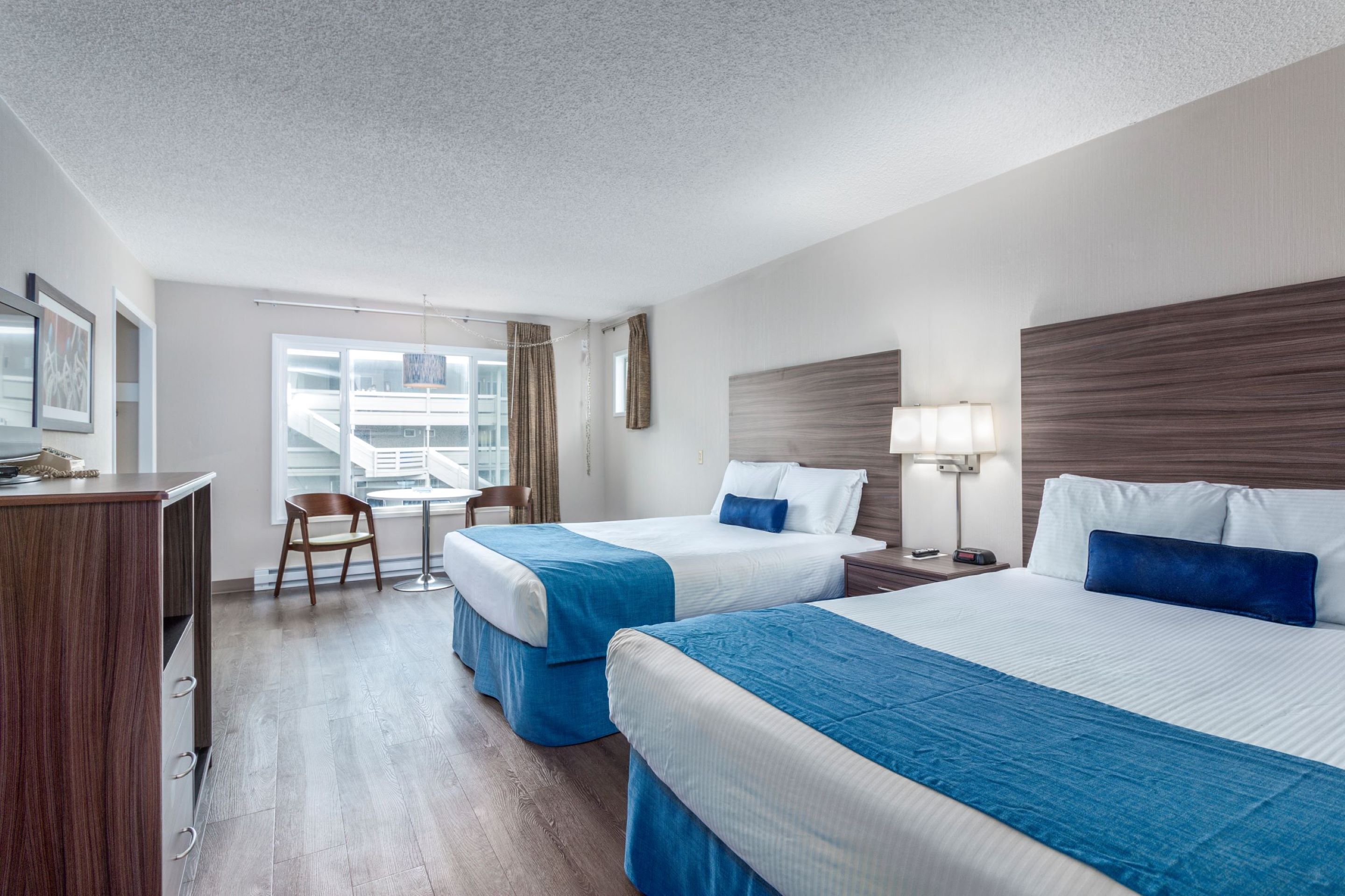 A hotel room with two beds, a desk, a chair, and a window with curtains.