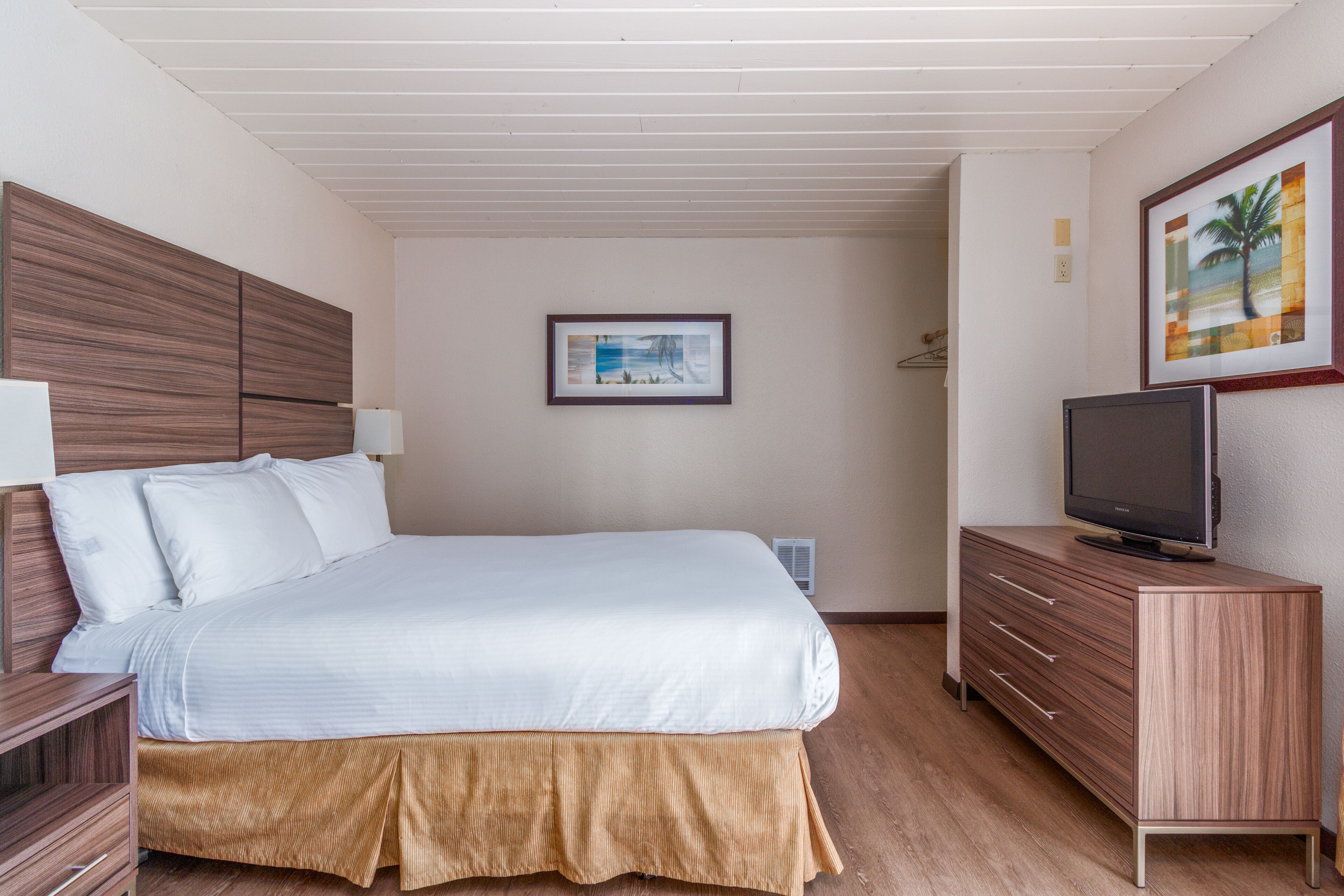 A hotel room with a bed, a TV on a dresser, and a framed picture on the wall.