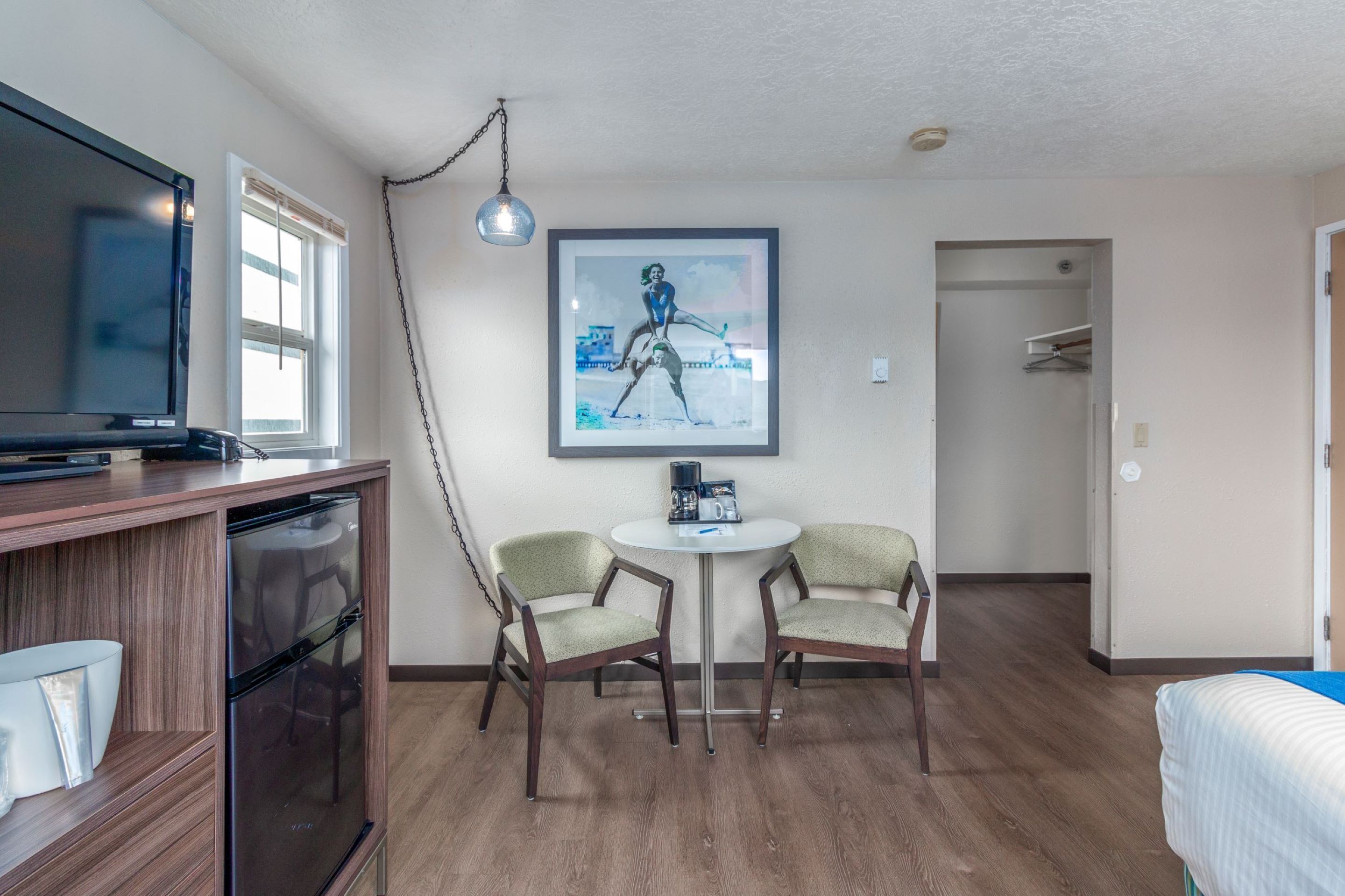 A hotel room with a wooden cabinet, a television, two chairs, a small table, and a framed picture on the wall.