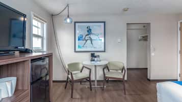A hotel room with a wooden cabinet, a television, two chairs, a small table, and a framed picture on the wall.