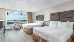 A hotel room with two beds, a desk, a chair, and a large window with a view. - Seashore Inn on the Beach (Seaside)