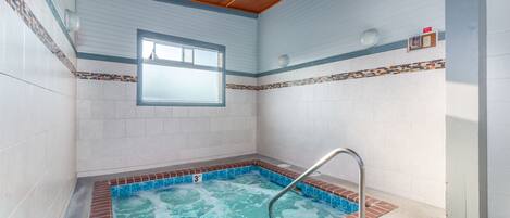 Una pequeña piscina interior con una escalera metálica, rodeada de paredes de azulejos blancos y techo de madera.