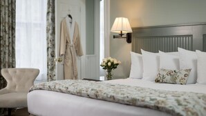 A hotel room with a bed, a chair, a lamp, and a vase with flowers.