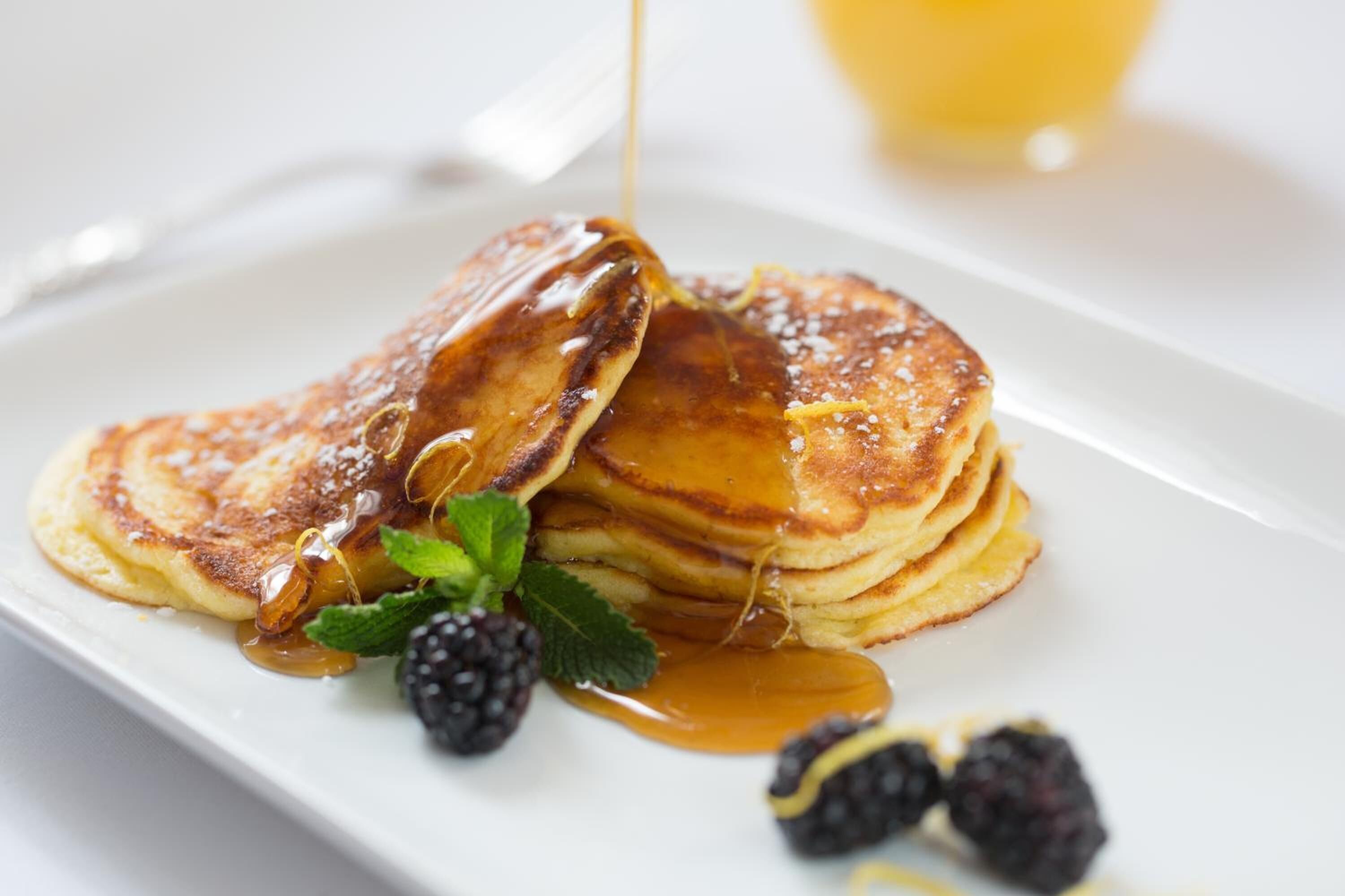 Une pile de crêpes nappées de sirop et garnies de mûres, le tout présenté sur une assiette blanche.