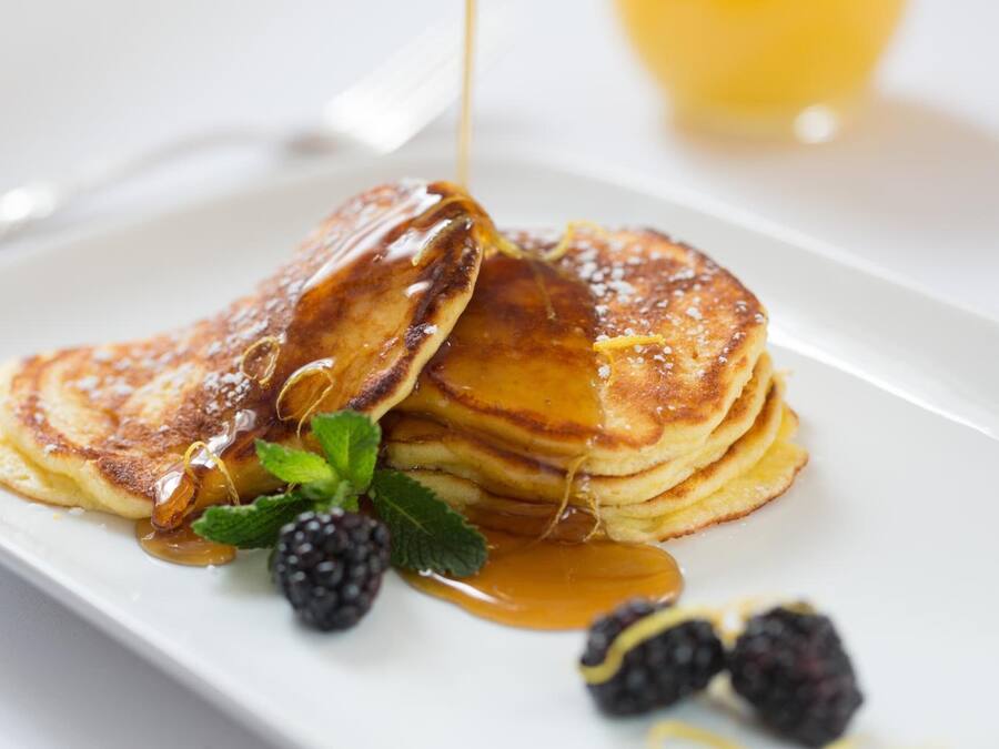 A stack of pancakes with syrup and blackberries on a white plate.