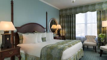 A neatly arranged hotel room with a large bed, two bedside tables with lamps, a chair, a small table with a vase, and a window with curtains.
