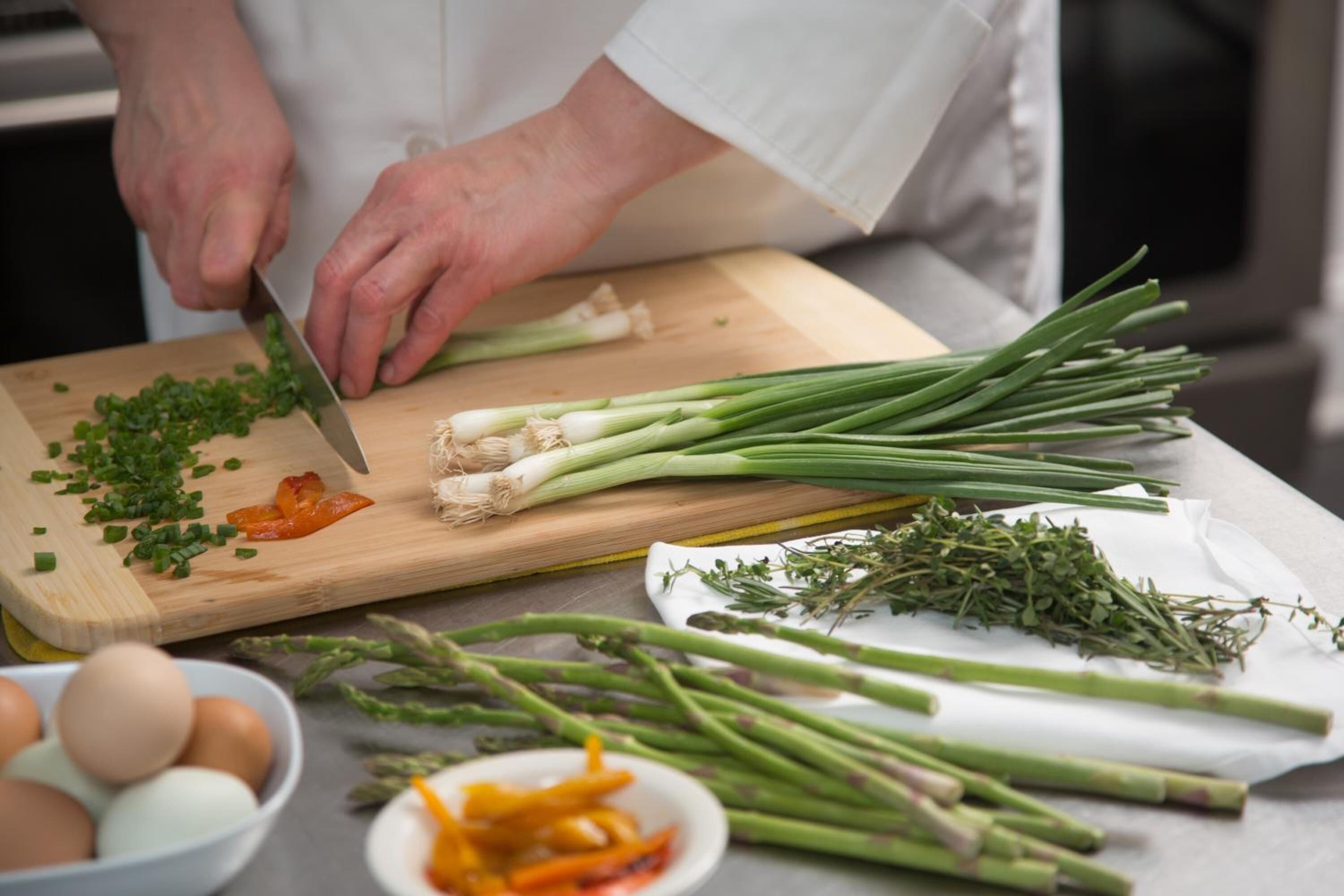 Un chef hache des oignons verts sur une planche à découper en bois.
