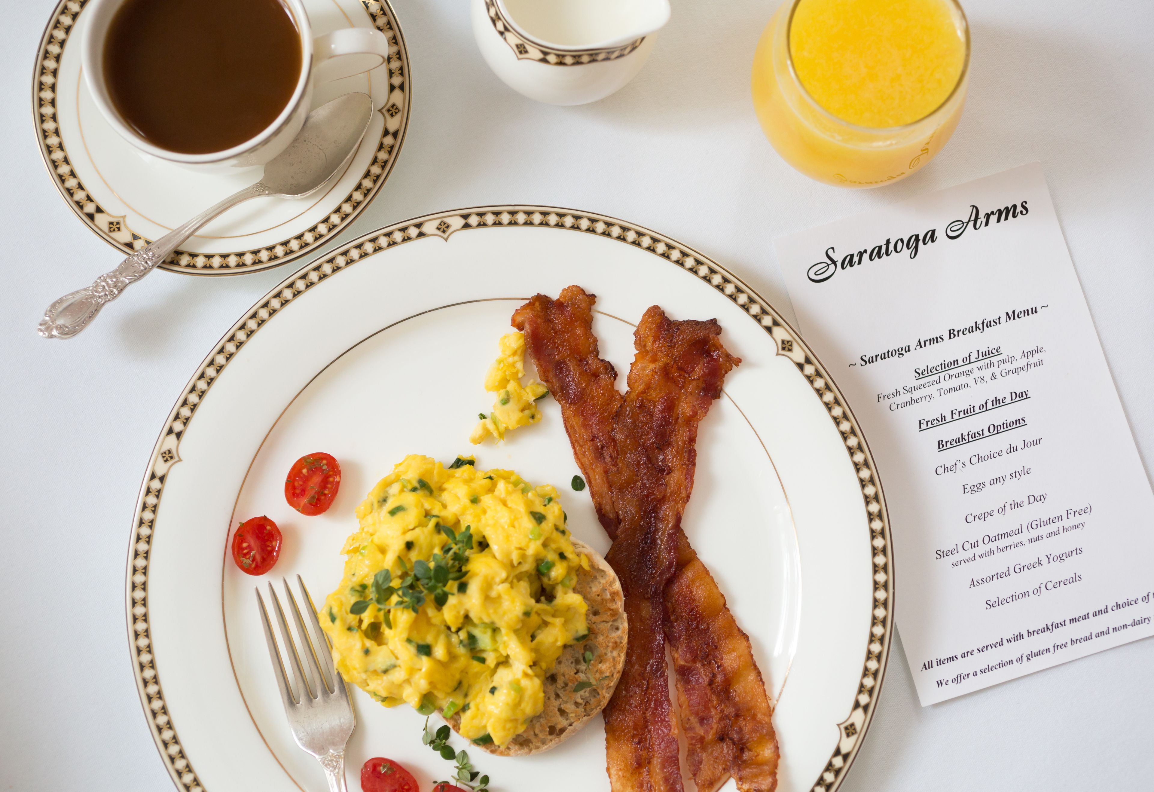 En frukosttallrik med äggröra, bacon och körsbärstomater, en kopp kaffe, ett glas apelsinjuice och en meny.