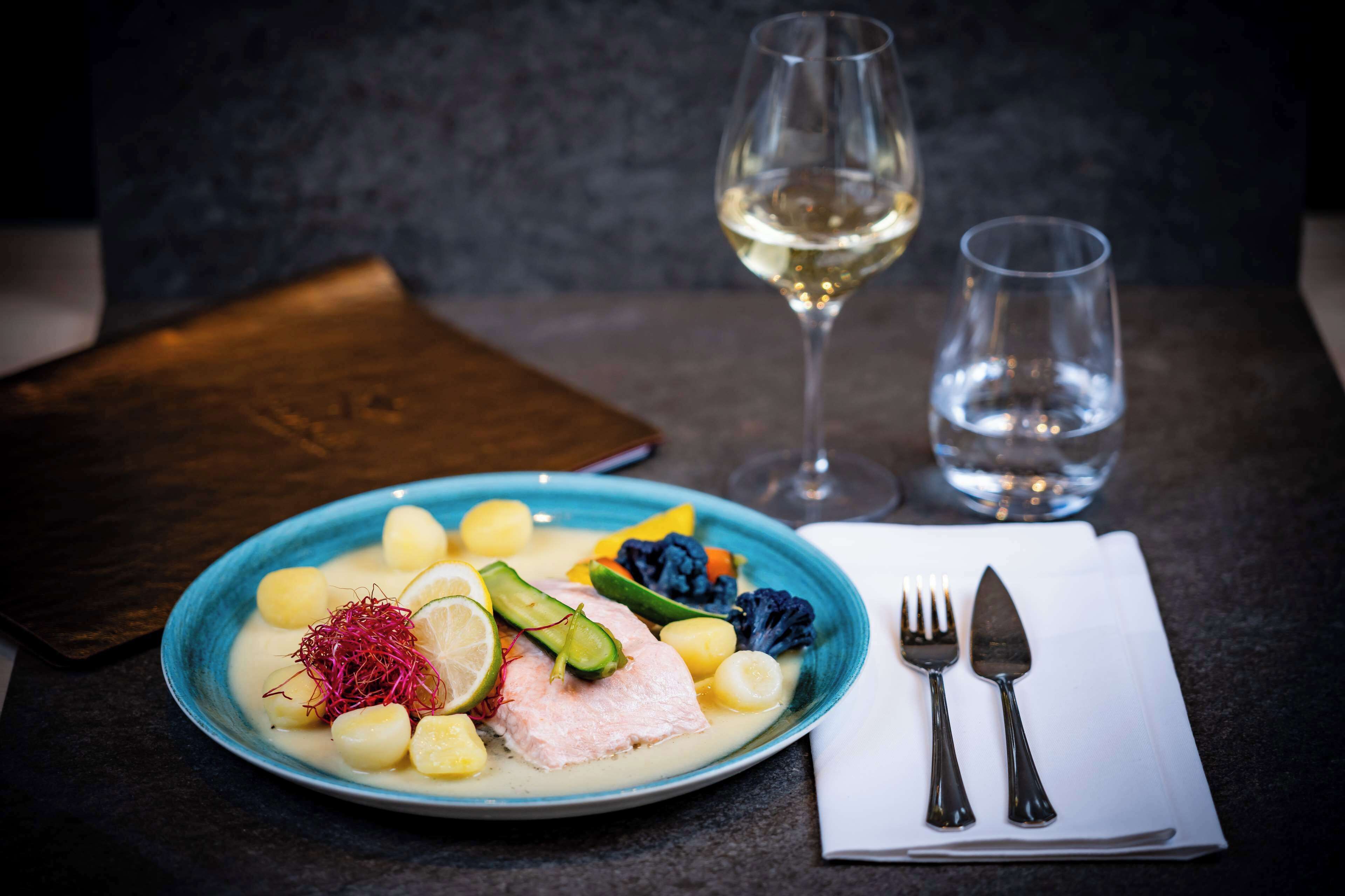 A plate of food with a fork and knife on a napkin, a glass of white wine, and a glass of water on a table.