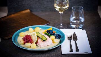 A plate of food with a fork and knife on a napkin, a glass of white wine, and a glass of water on a table.