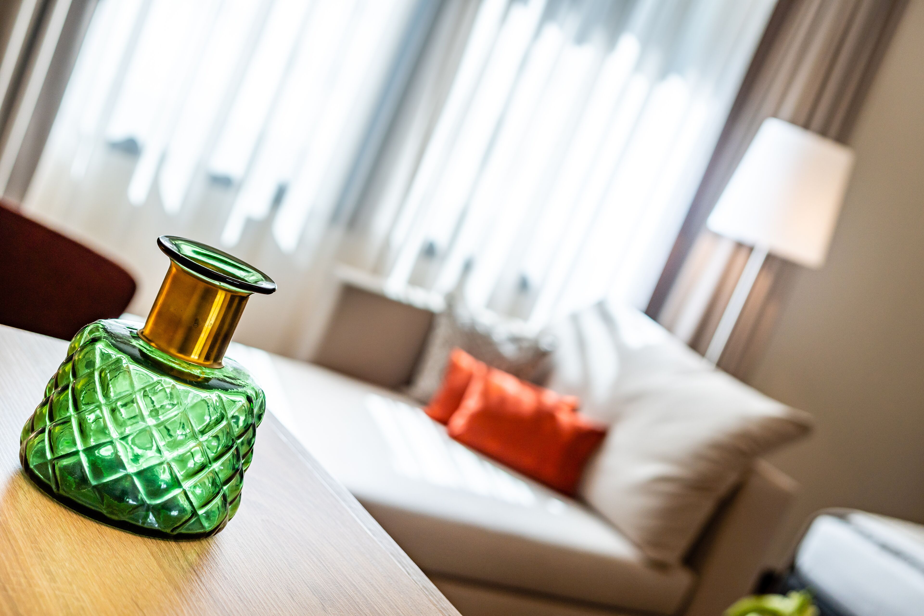 Een groene decoratieve fles op een houten tafel in een kamer met een witte bank en een rode kussen.