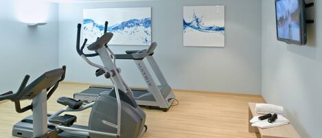 A gym with two treadmills, a stationary bike, and a bench with towels and a water bottle.