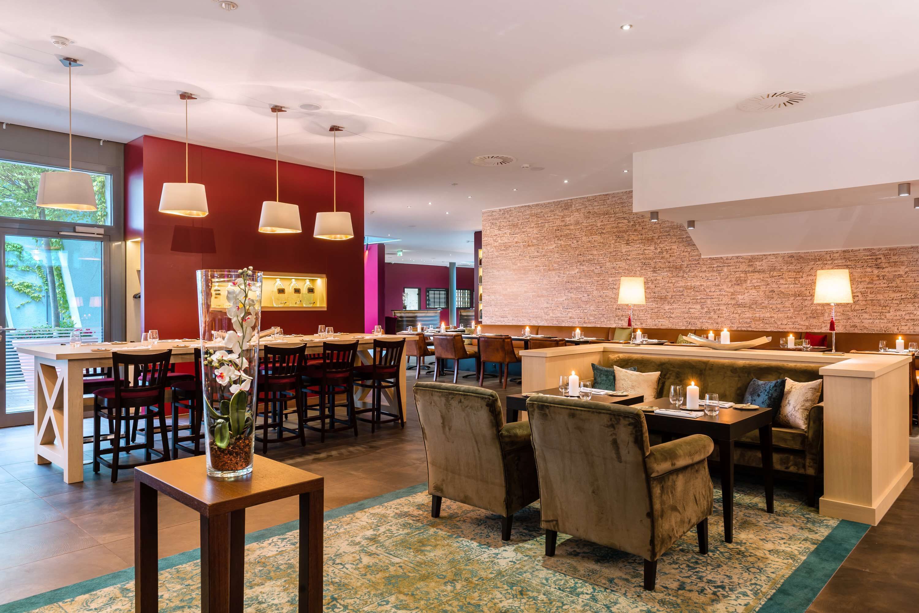 A restaurant with a brick wall, hanging pendant lights, and a central seating area with cushioned chairs and tables.