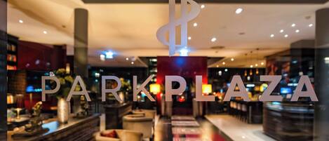 Un interior moderno del Park Plaza, con una zona de bar, asientos y una escalera visible.