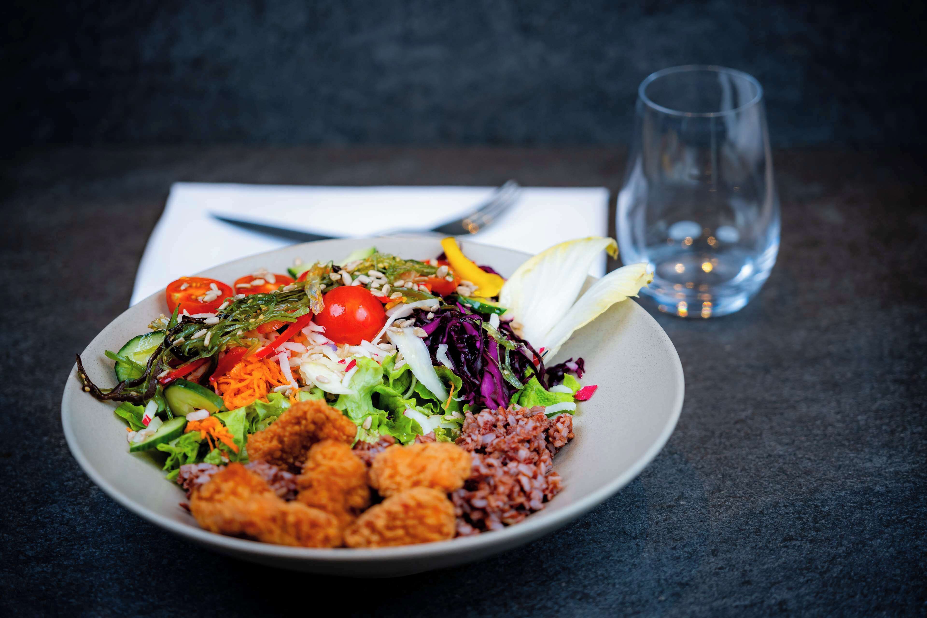 A plate of food with various vegetables and a glass of water on a dark surface.