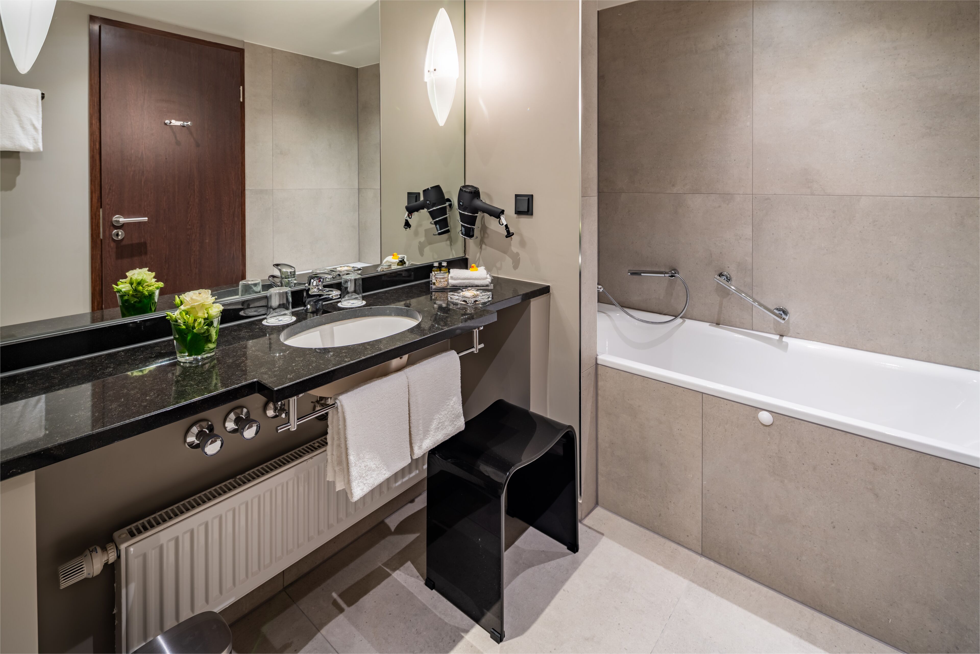 Une salle de bain moderne avec un meuble-lavabo à deux vasques, un grand miroir, un sèche-cheveux, un porte-serviettes et une baignoire.