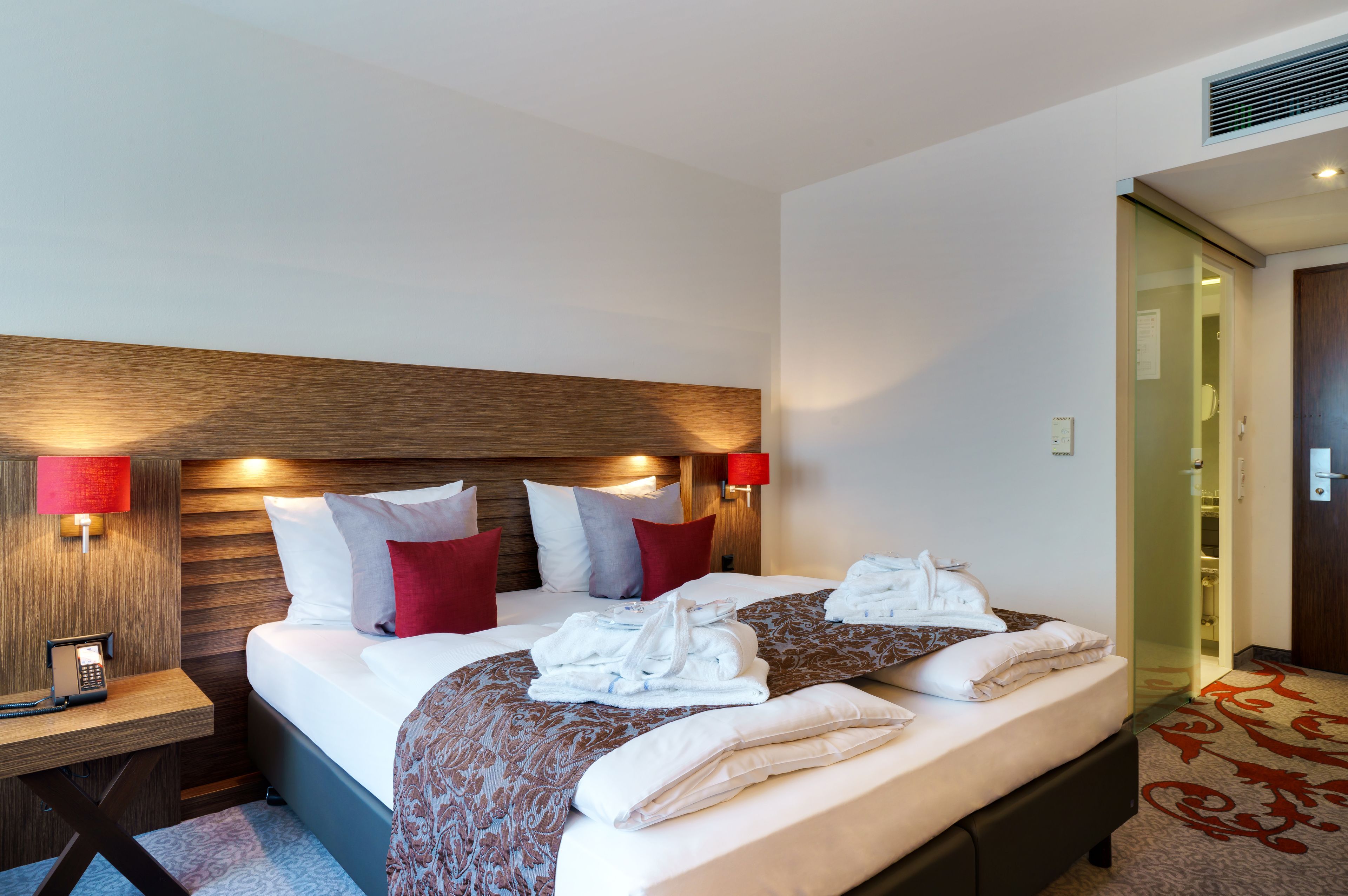 A hotel room with a large bed, two bedside tables, a telephone, and a red wall lamp.