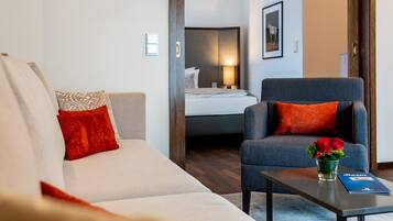 A modern hotel room with a sofa, armchair, and a small table with a vase of flowers.