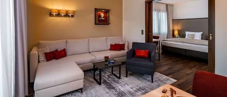 A modern hotel room with a sofa, armchair, and a small table with dominoes.