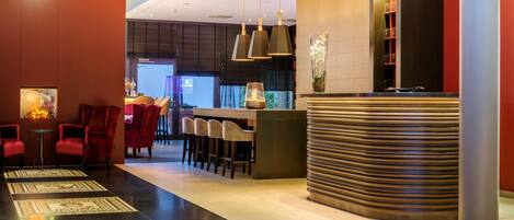 A modern hotel lobby with a reception desk, bar area, and seating.