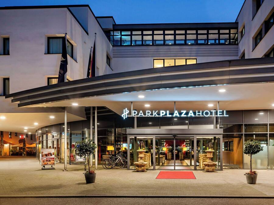 The exterior of the Dark Plaza Hotel with a modern design, featuring a prominent entrance, glass doors, and a red carpet leading to the lobby.