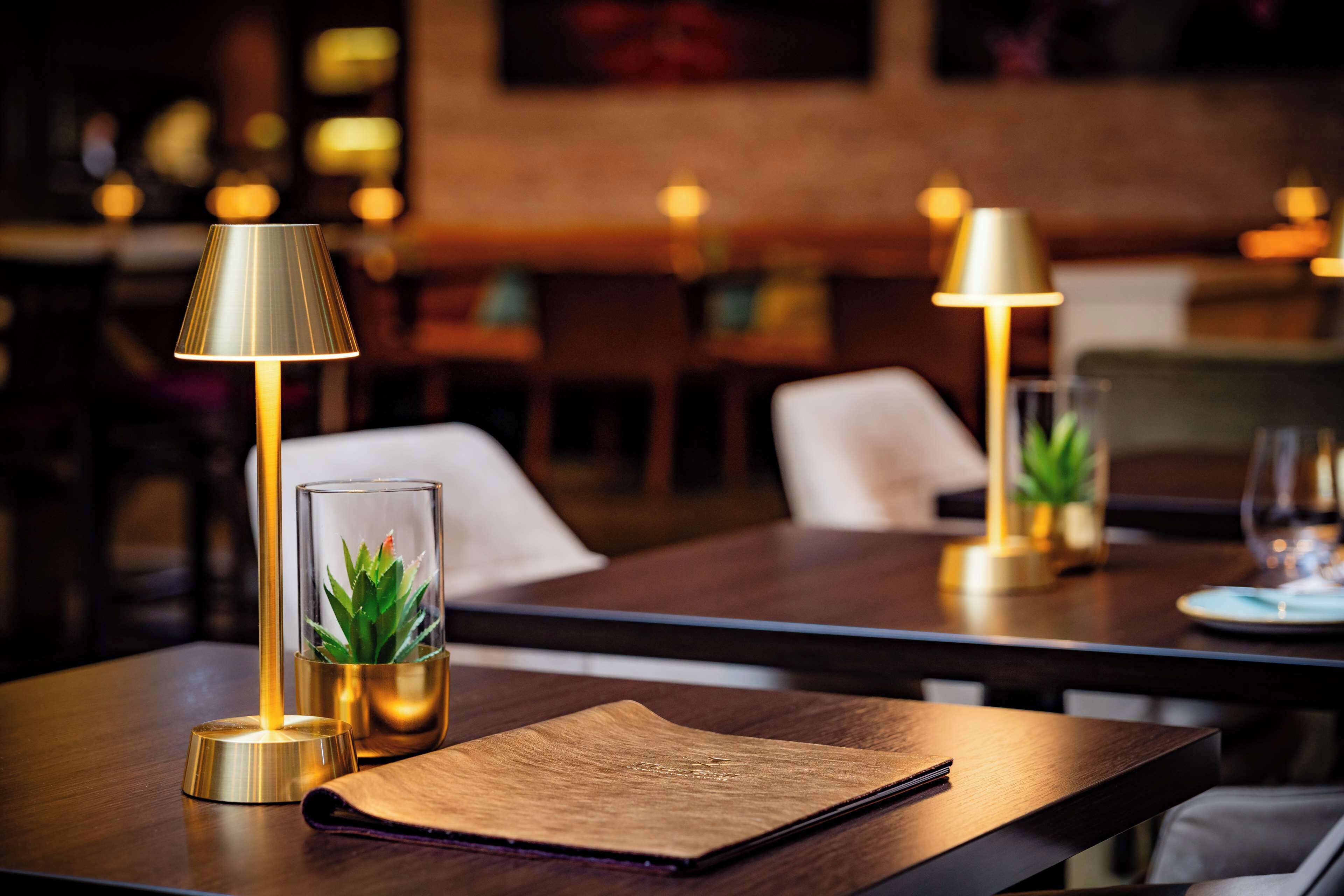 Ein Restauranttisch mit einer Lampe, einem Glasgefäß mit Pflanze und einer Speisekarte.