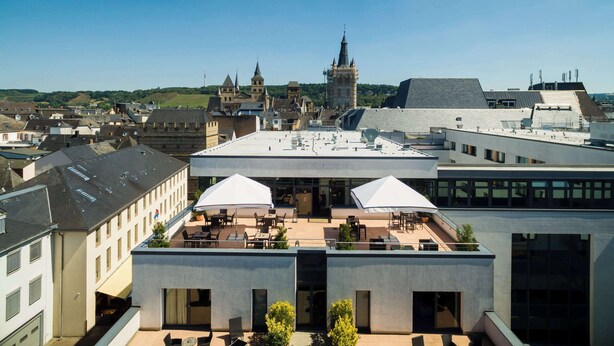 A rooftop terrace with outdoor seating and a view of historic buildings in the background. - Park Plaza Trier (Trier)