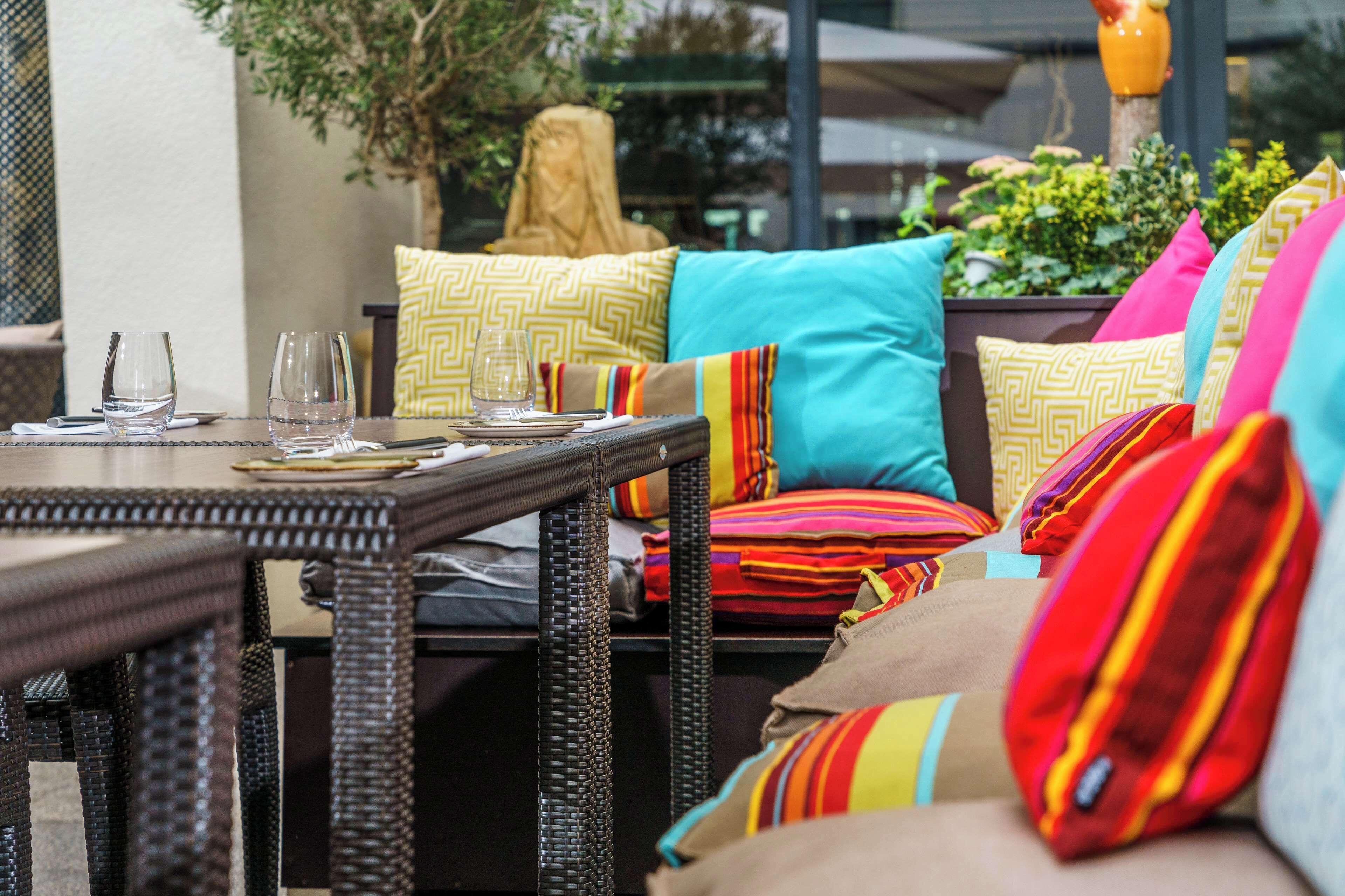 A dining area with a wicker table, colorful cushions, and a glass of water.