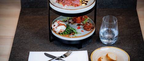 A three-tiered serving tray with various dishes, a glass of water, and a plate with bread slices on a table.
