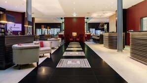 A hotel lobby with a central seating area, a reception desk, and a bar. - Park Plaza Trier (Trier)