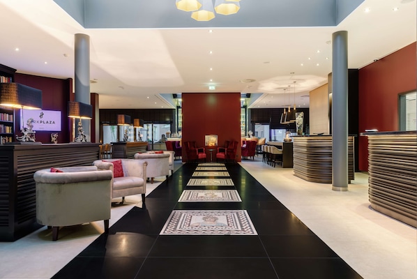 Un vestíbulo de hotel con una zona de estar central, un mostrador de recepción y un bar.