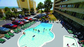 Un espace piscine sur le toit, comprenant plusieurs piscines, des chaises longues et un parking avec des voitures.