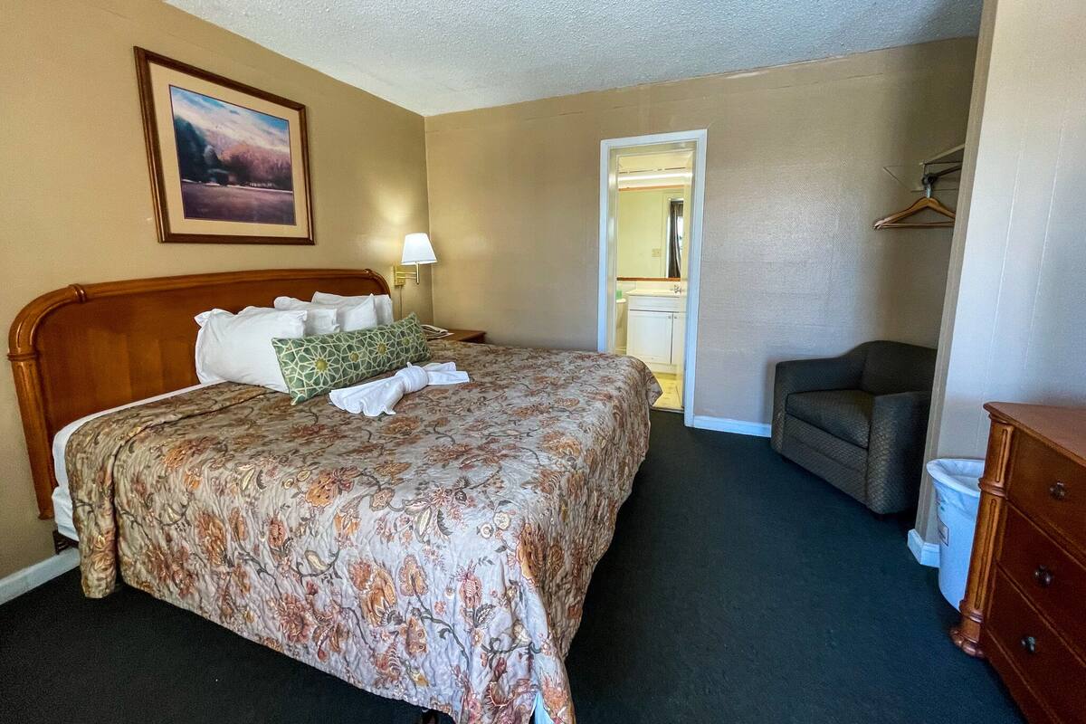 A hotel room with a large bed, a chair, a dresser, and a bathroom visible through an open door.