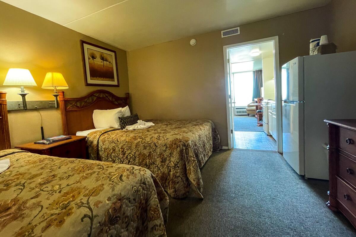 A hotel room with two beds, a dresser, and a refrigerator.