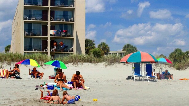 Un hôtel à plusieurs étages doté de balcons, situé sur une plage de sable.