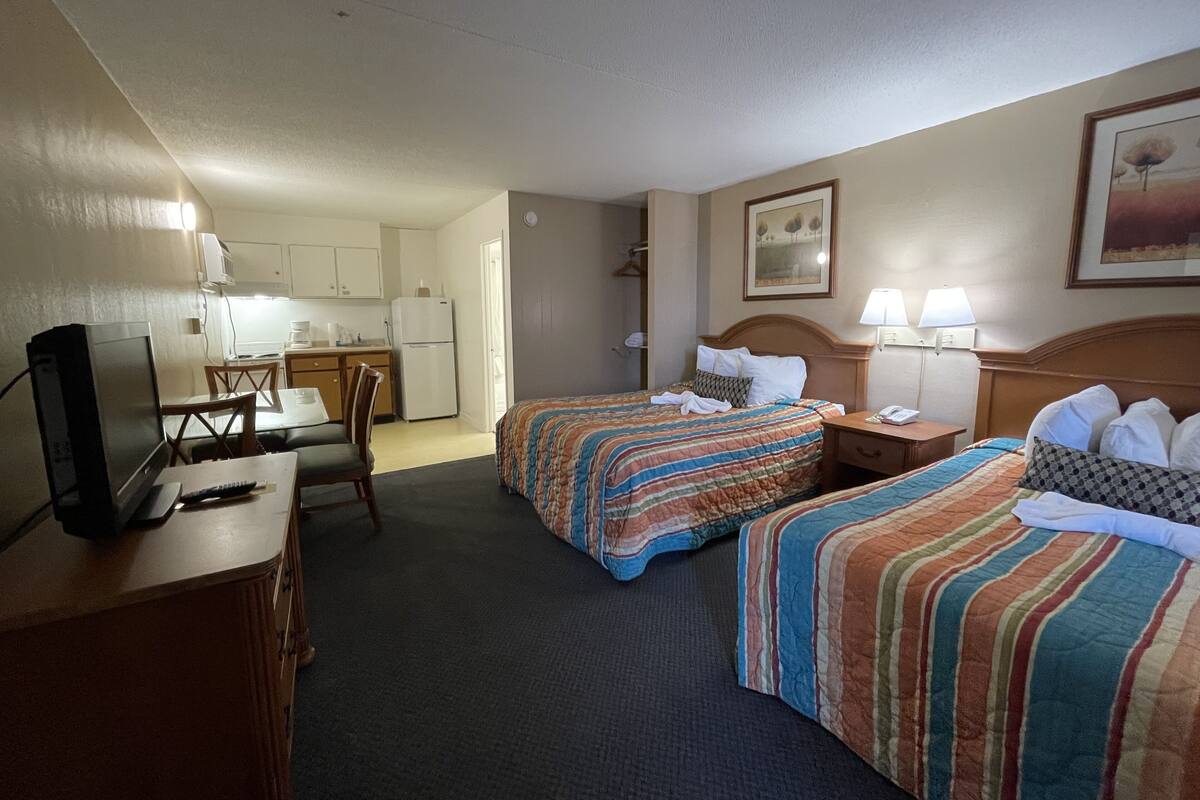 A hotel room with two beds, a desk with a computer, a chair, and a kitchenette.