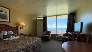 Une chambre d’hôtel avec un lit, deux fauteuils, une télévision et une vue sur la plage.