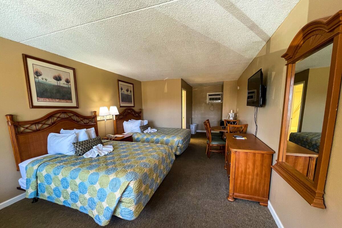 A hotel room with two beds, a desk, a chair, a TV, and a mirror.