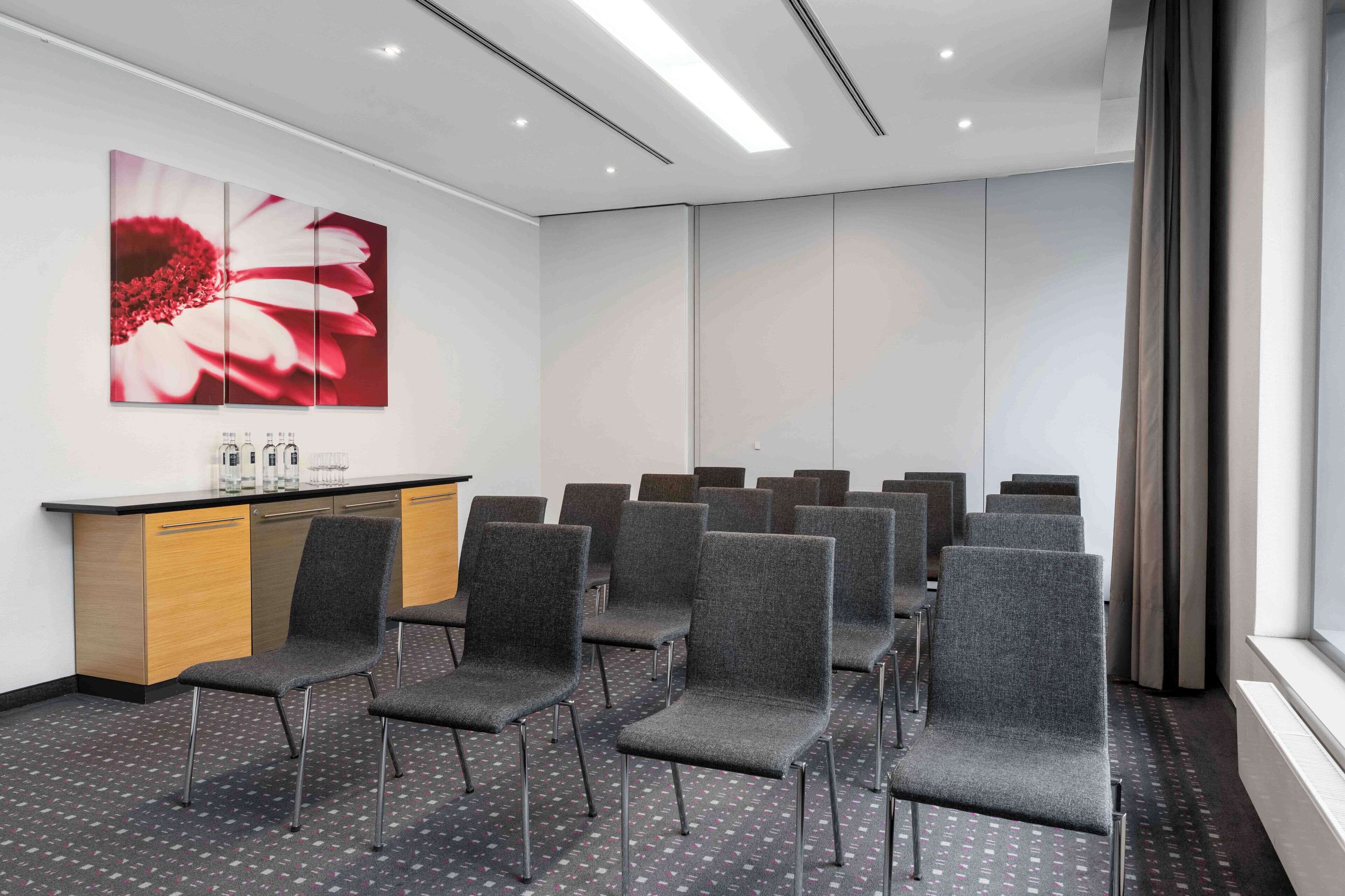 A conference room with grey chairs, a wooden desk, and a large floral painting on the wall.