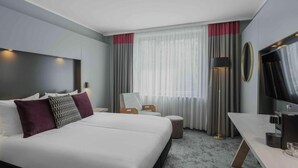 A modern hotel room with a large bed, bedside tables, a desk, a chair, a TV, and a window with curtains. - Ramada by Wyndham Essen (Essen)