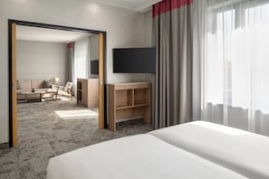 A hotel room with a bed, a desk, a chair, a TV, and a view of the outside through the window. - Ramada by Wyndham Essen (Essen)
