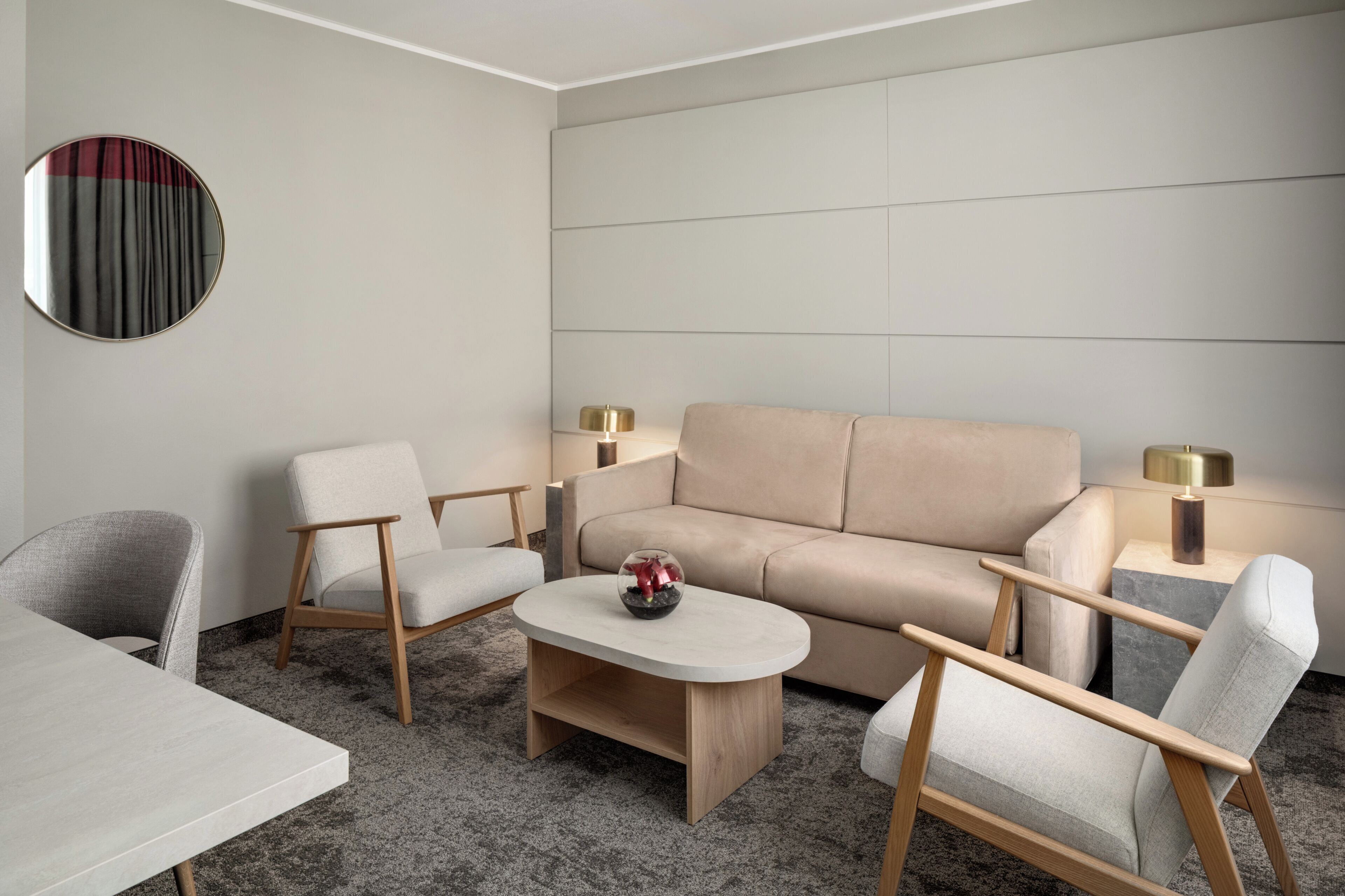 Een moderne woonkamer met een bank, twee fauteuils, een salontafel en twee bijzettafels met lampen.