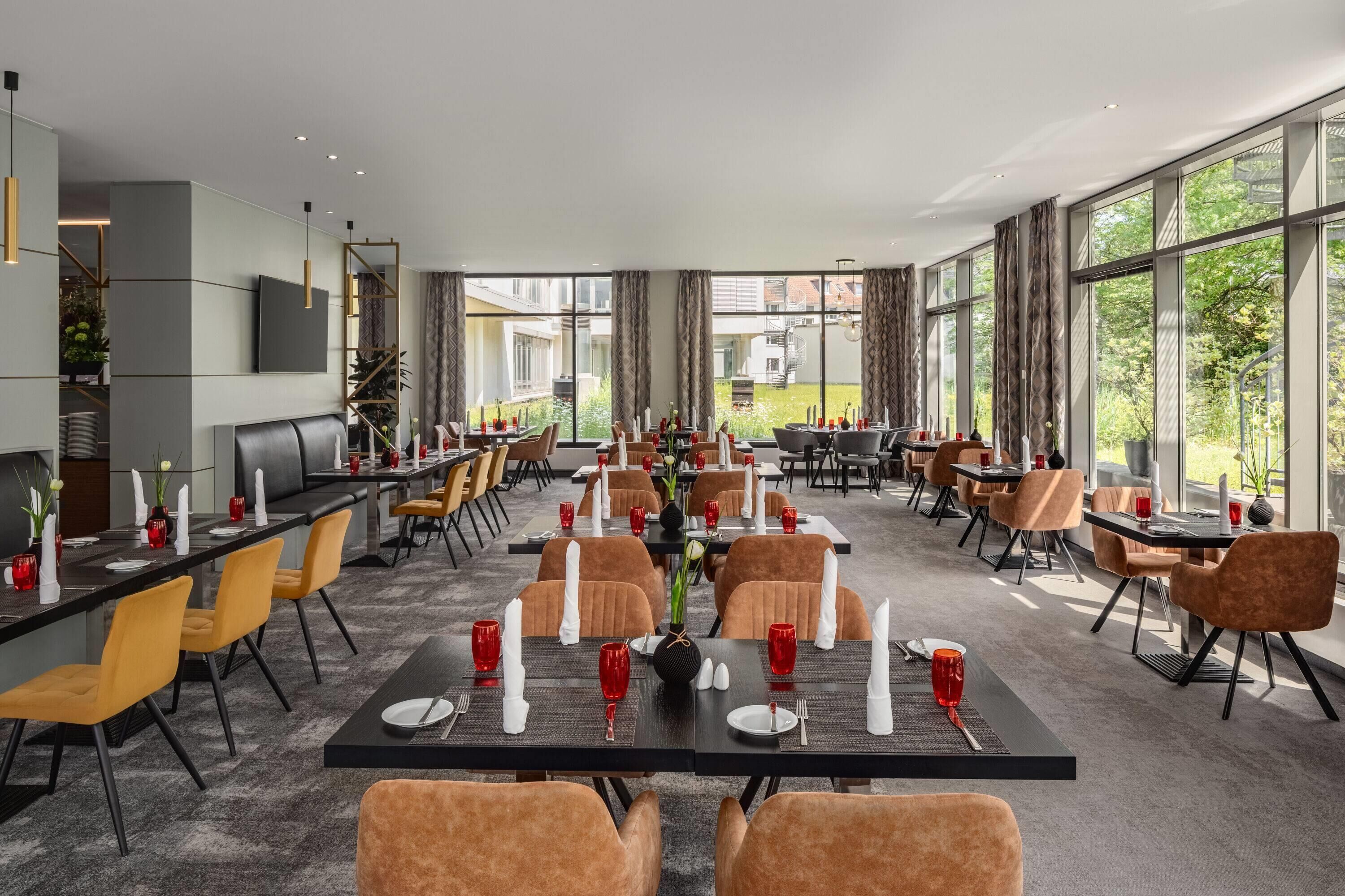 A spacious dining area with multiple tables and chairs, large windows offering views of the outdoors, and a modern interior design.