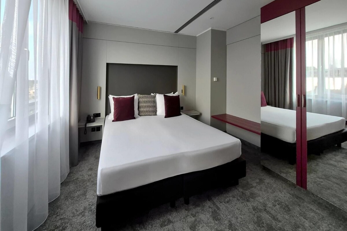 A modern hotel room with a large bed, bedside tables, a nightstand, and a mirror.