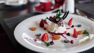 Un plato de postre con diversas frutas y bayas, acompañado por una taza y un platillo al fondo.